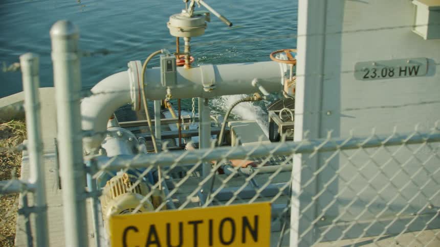 Large pipes and mechanical pumps extend from a building located at the waters edge in this dolly shot looking down