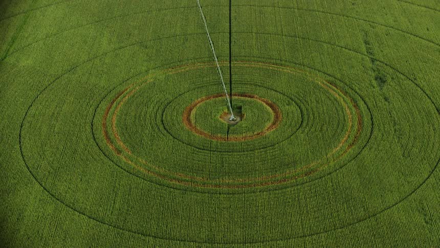 An aerial view of a large corn field being irrigated by a center pivot sprinkler system shot from a high speed aircraft eventually tilting up to reveal the rural farm