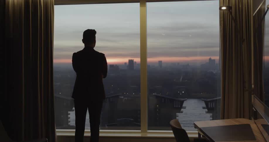 A man watches the sun set over downtown from his high rise apartment