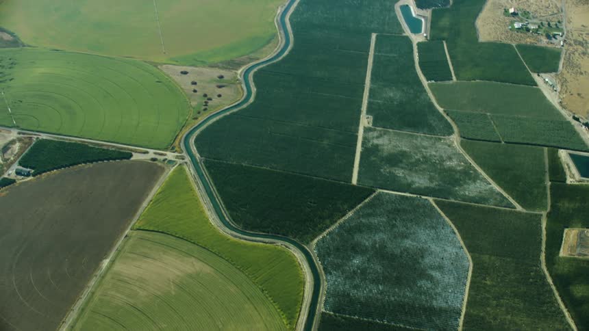 An aerial view of an irrigation canal weaving through varied symmetries of farm and agriculture land as the camera tilts up revealing the vast valley