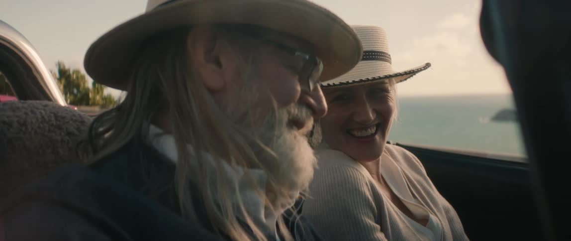 A man and a woman are sitting inside a convertible automobile smiling and laughing