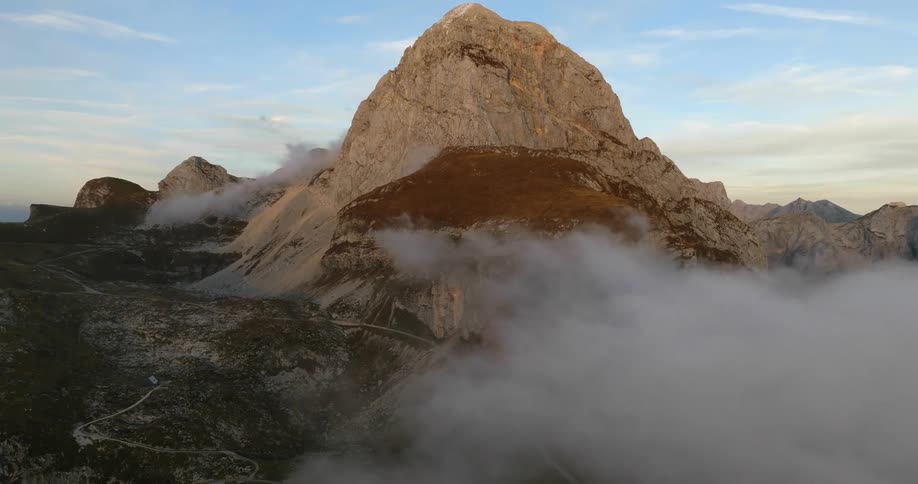 A tall rocky mountain towers high above the nearby clouds
