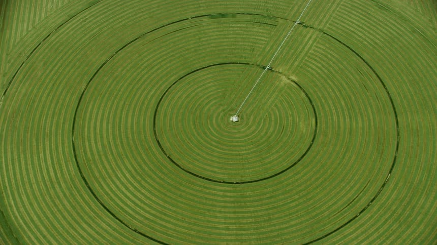 The camera flies over and tilts down perfectly center on the vast center pivot crop being grown
