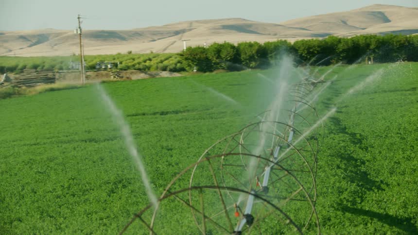 Aerial shot of irrigation sprinklers spraying massive amounts of precious water on a green field in a dry desert valley