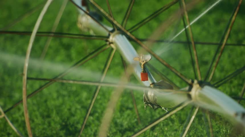 Tight slowmotion shot of irrigation sprinklers watering an alfalfa field in the arid US