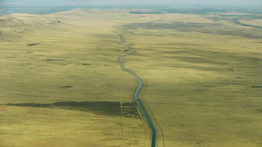 The camera tilts up revealing a vast and miles long irrigation canal as it weaves through a stark and arid desert landscape