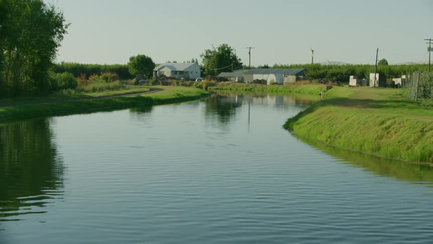 An irrigation canal runs through a rural farm zone in the arid western United States