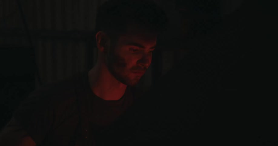 Red glowing flames flicker off a mans face in a dark room