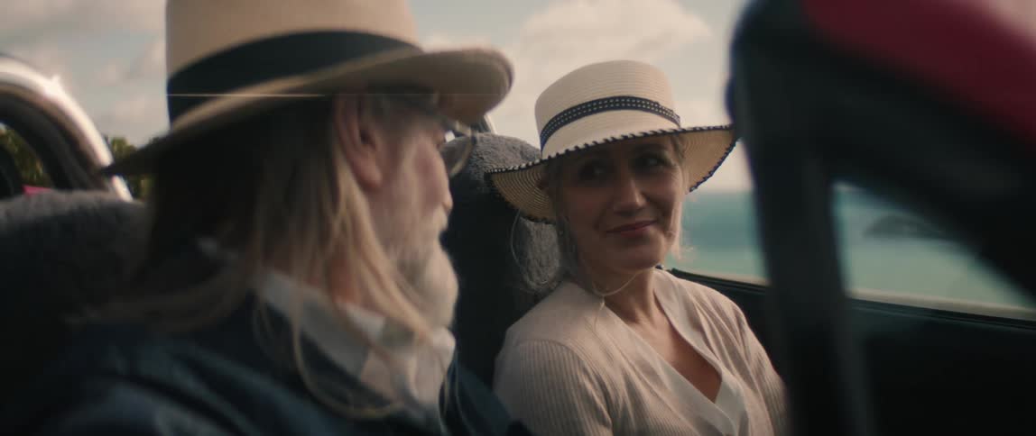 A woman sits down in a convertible car while chatting with her male companion