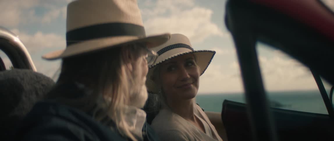 Woman wearing hat earrings and white shirt gets in convertible car next to elderly man with hat glasses long hair and beard