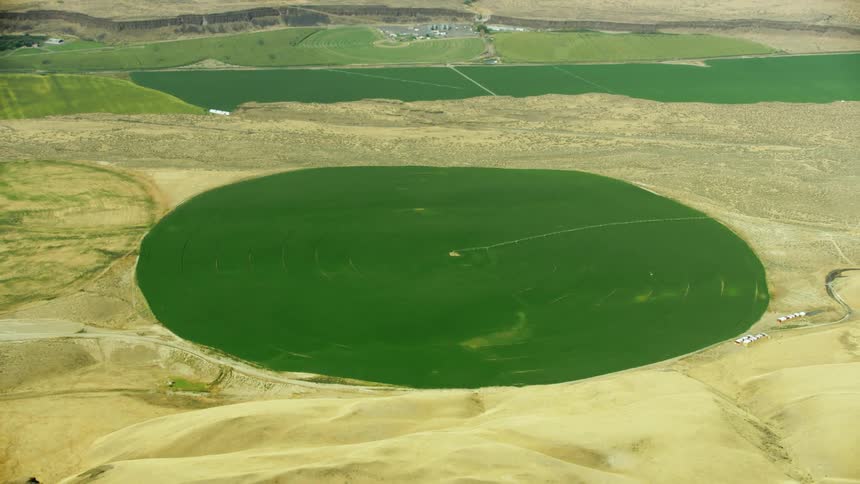 High altitude aerial tilting up revealing the contrast between irrigated and non-irrigated dry desert land in the western USA