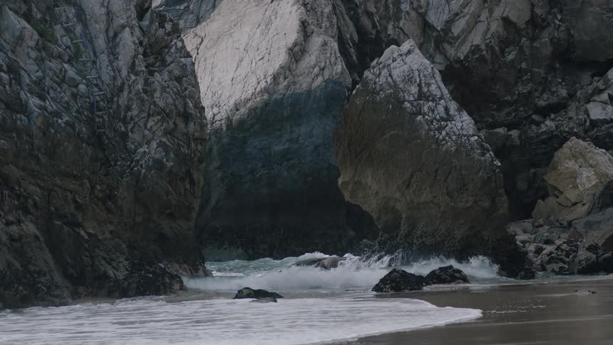 Water coming ashore on a beach with large rock formations