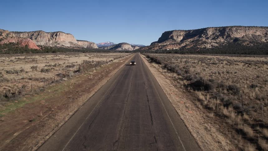 A car races down a road with mountains in the distance