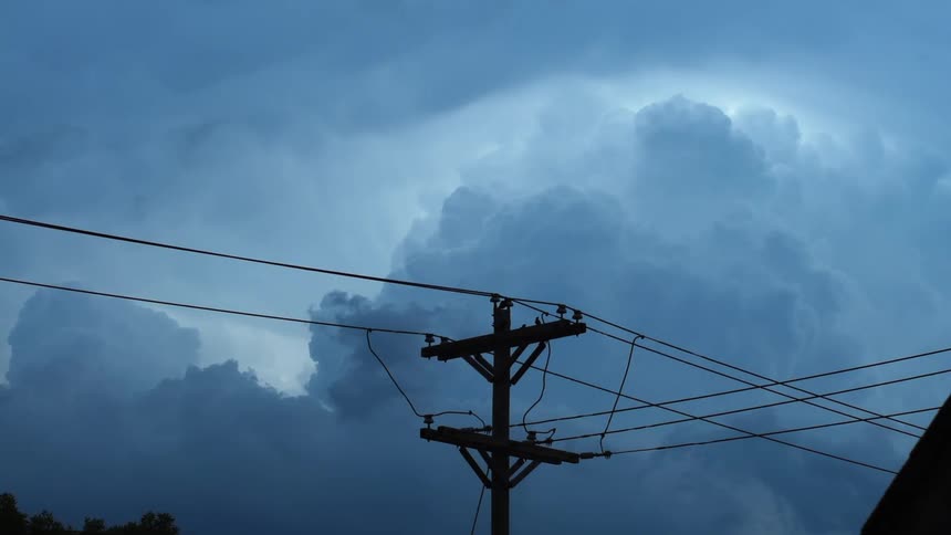 Cables stretch across utility poles as clouds move in the sky above