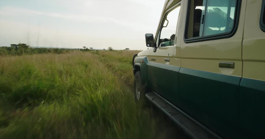 A large vehicle travels offroad through a grassland during the day