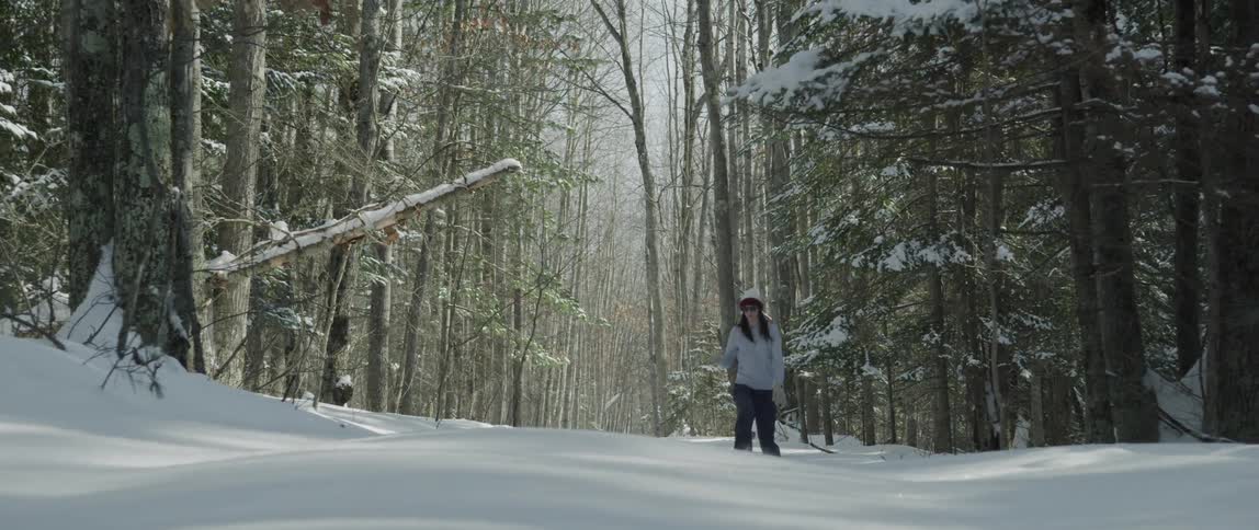A woman walks through knee high snow in the forest