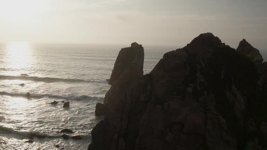 Large rock formations near a mountainous coast line at dawn