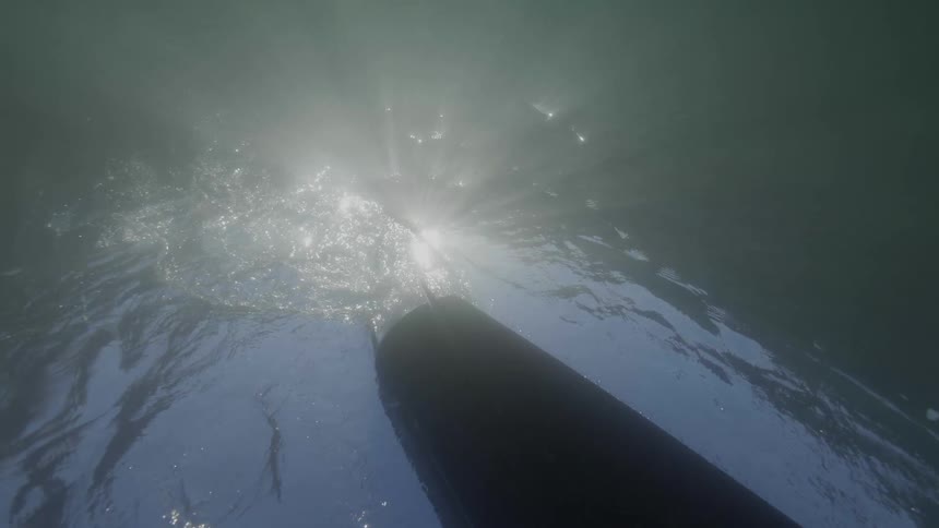 View from underwater looking up as the sun shines over the water a rowboat passes overhead