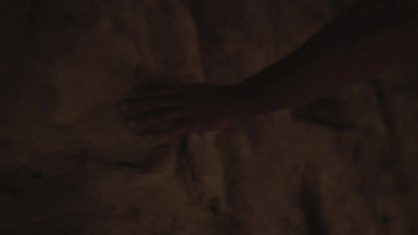 A person runs their hands across a stone wall