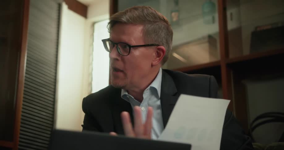 A man holds a sheet of paper with graphs while discussing them extensively