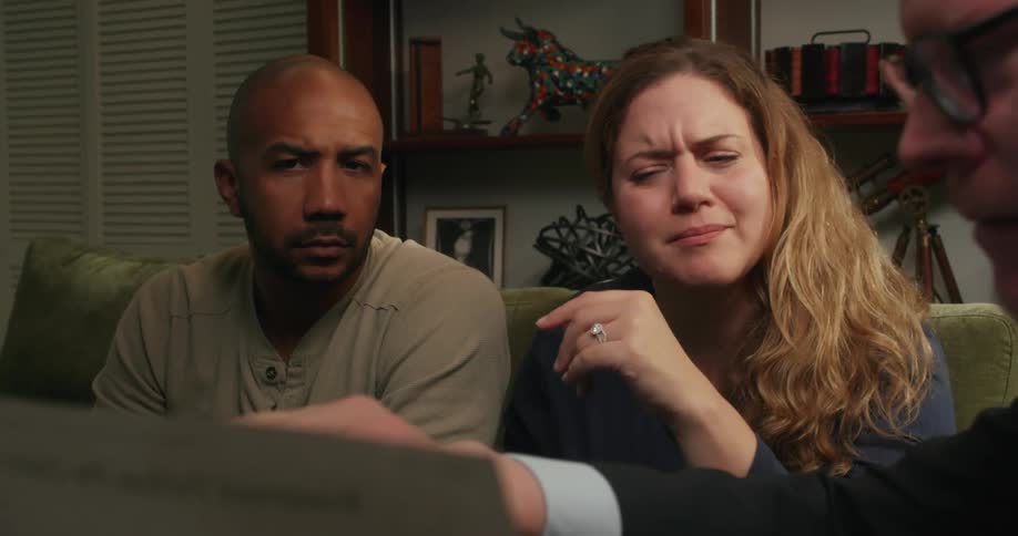 Three people having a conversation while looking at a document and sitting on a living room sofa