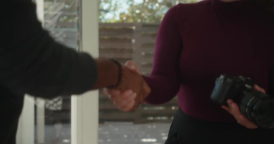 A woman holding a camera shakes hands with a man