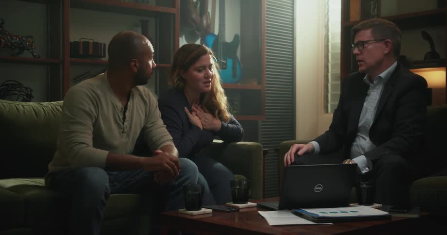 Three people are sitting in a living room with a laptop computer on the table and talking to each other