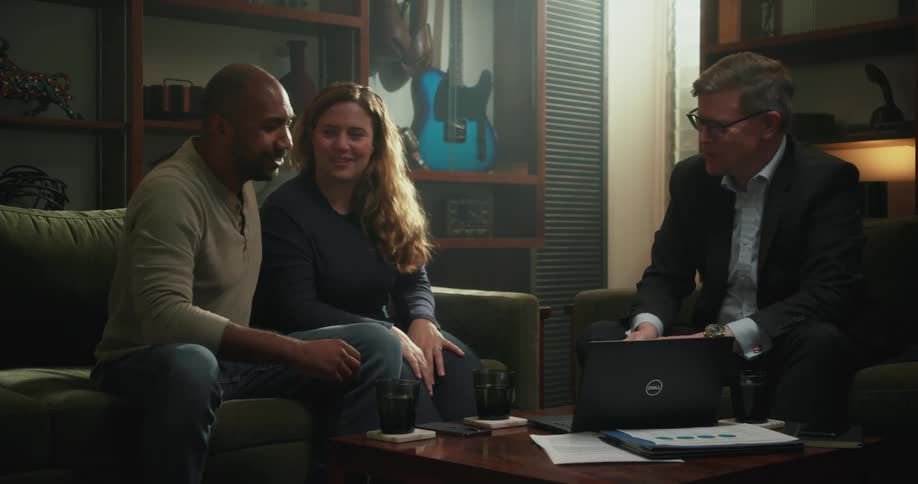 Couple makes up holding each other next to man wearing glasses and blazer jacket looking at laptop in living room at home