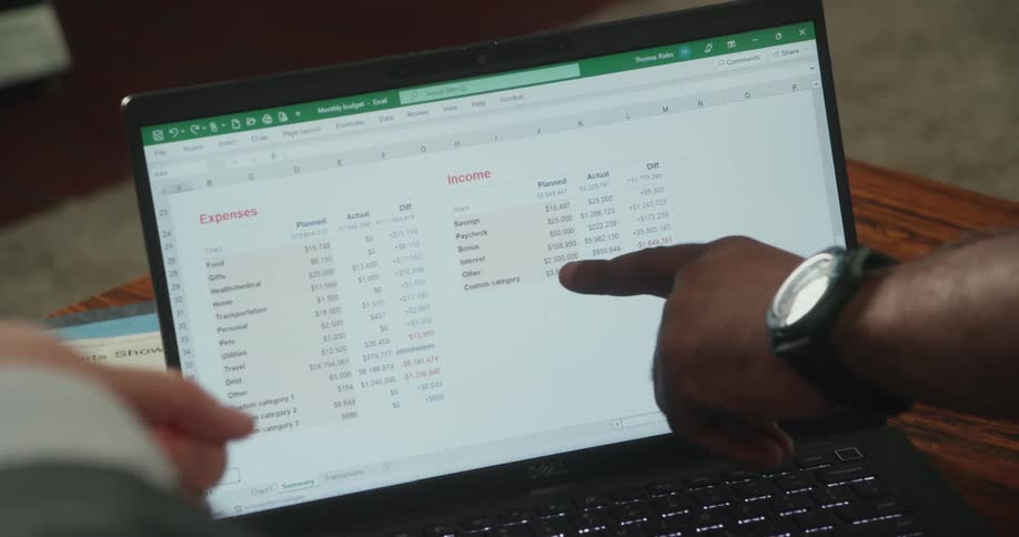 Two men point at numbers on a spreadsheet being displayed on a laptop