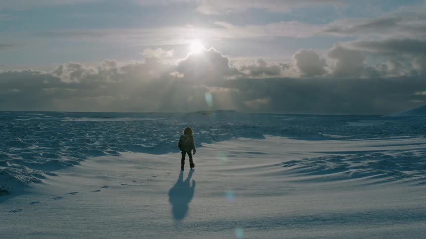 A lone human in heavy arctic apparel walks through a freezing snowcovered landscape