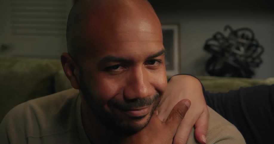 A man is smiling and talking as he sits on a couch and kisses a female hand