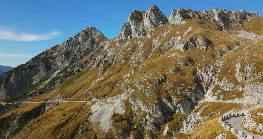 A rocky mountain range has a single road that winds around its rocky edges