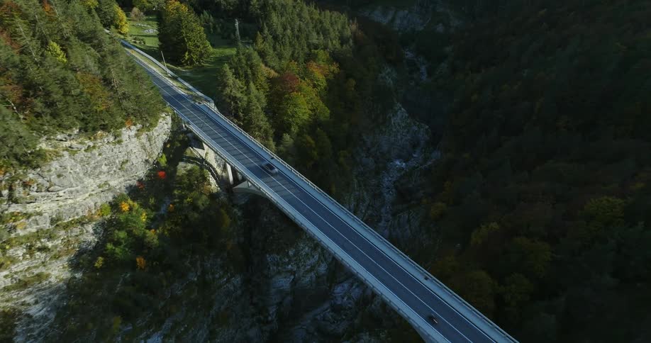 A narrow two lane roadway traverses a rocky canyon in a forested area