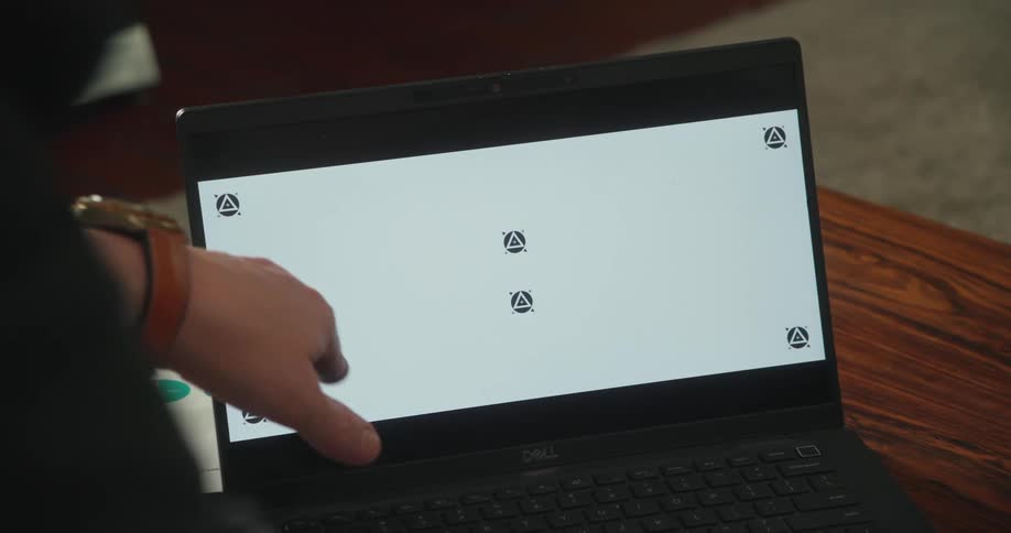 A person gestures at the screen of a laptop resting on a table
