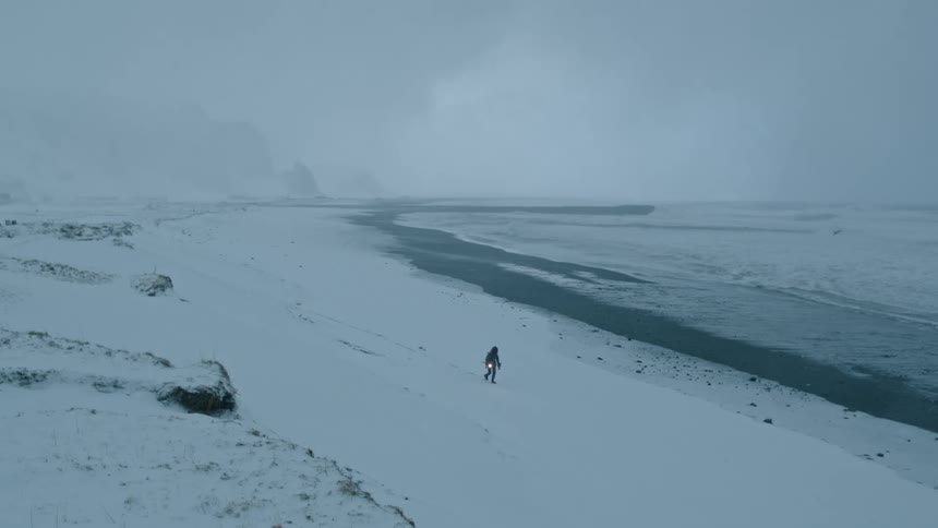 A person walks on the snow covered shore