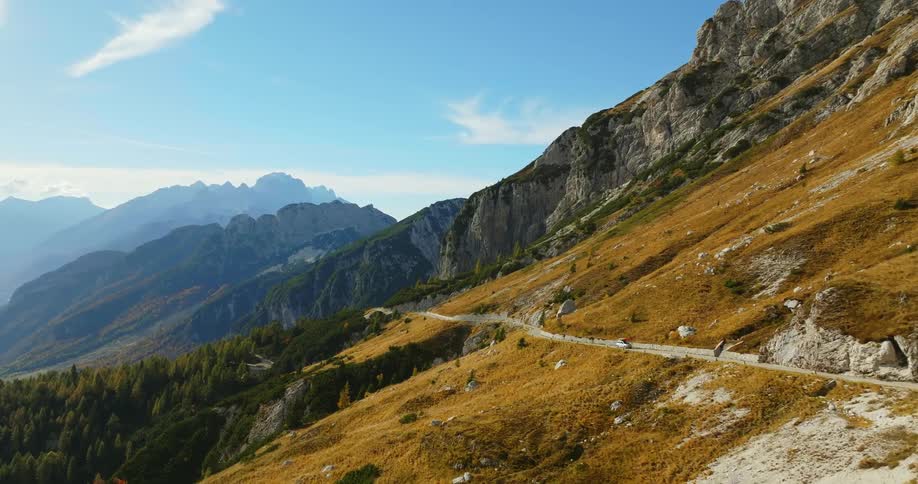 Aerial view of faraway cyclists riding bicycles on mountain road passing by car