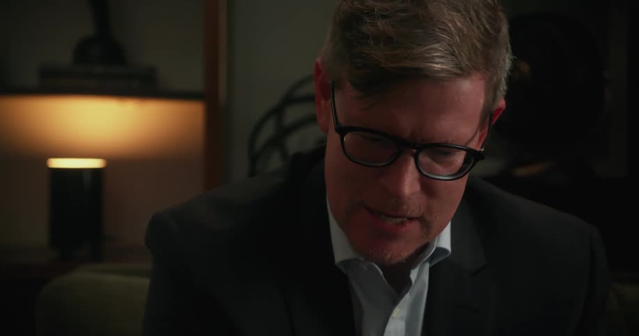 A man is wearing a suit and talking to someone indoors