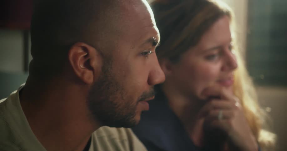 A man and a woman are sitting in the living room speaking to someone across the room