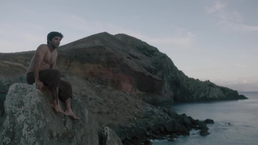 A man sits on a rock by the shore