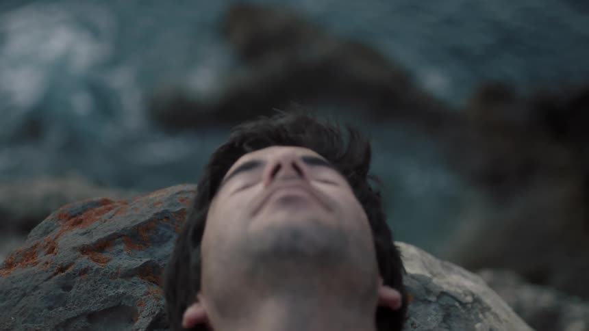 A man walks up as he is laying on the cliff by the shore
