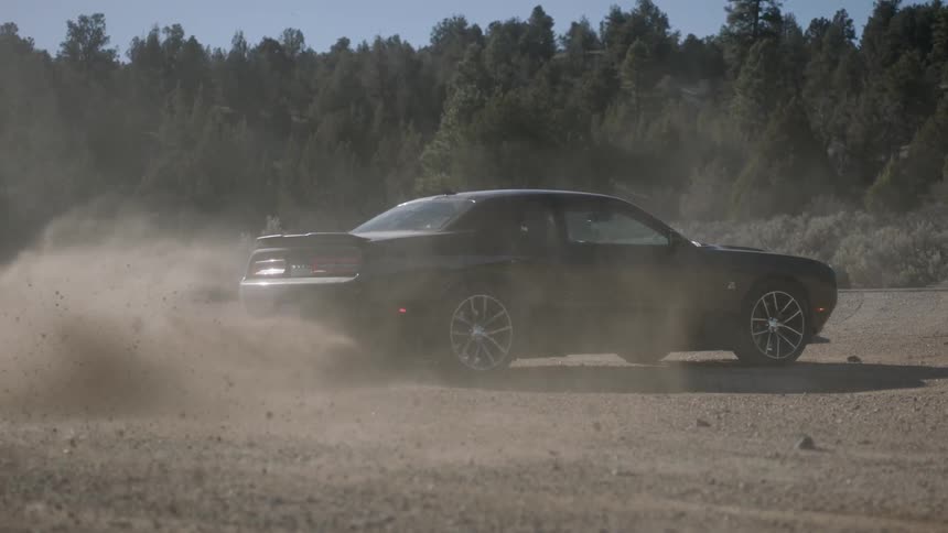 A modern muscle car spins out on dirt and gravel