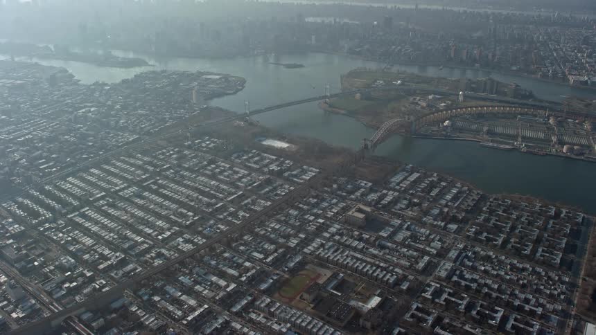 A birds eye view aerial footage that tilts up from urban neighborhoods to reveal bridges spanning the East River in Queens New York City during winter