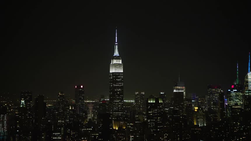 A stunning night-time aerial view of the iconic Empire State Building and Midtown Manhattan skyscrapers bathed in clear bright lights during a winter evening in New York City