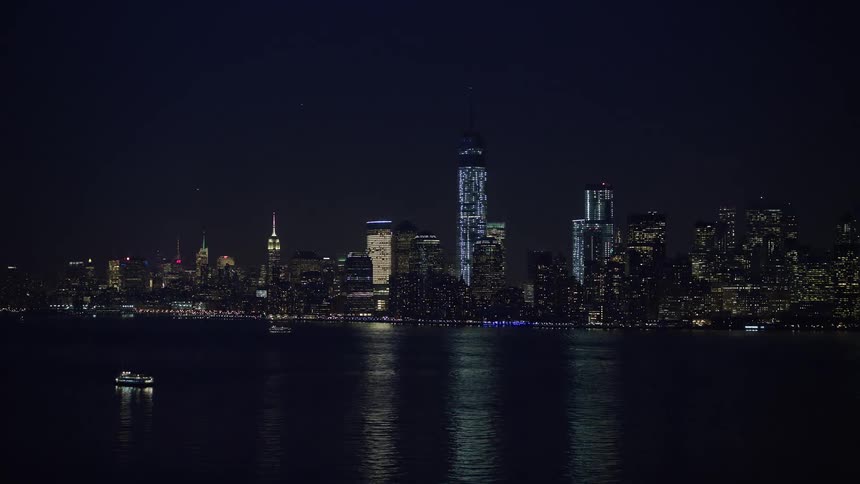 An aerial view of the statue of liberty flying towards the Lower Manhattan skyline of New York City at night during winter