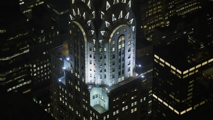 An aerial view of the iconic Chrysler Building and surrounding skyscrapers illuminated at night during winter in Midtown Manhattan