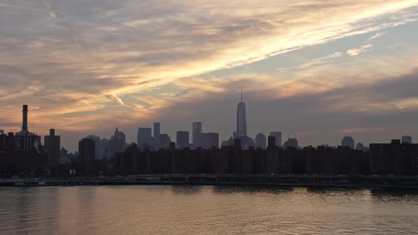 A low flying aerial shot of the Lower Manhattan skyline as seen from East River during winter sunset