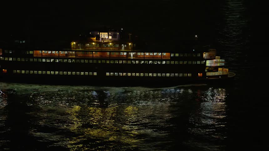 The Staten Island Ferry sails through a clear New York Harbor at night during winter captured in high-quality aerial footage