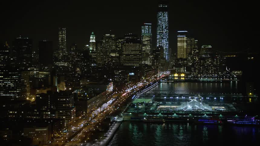 Approaching Lower Manhattan and Greenwich Village skyscrapers and piers illuminated by city lights on a clear winter night