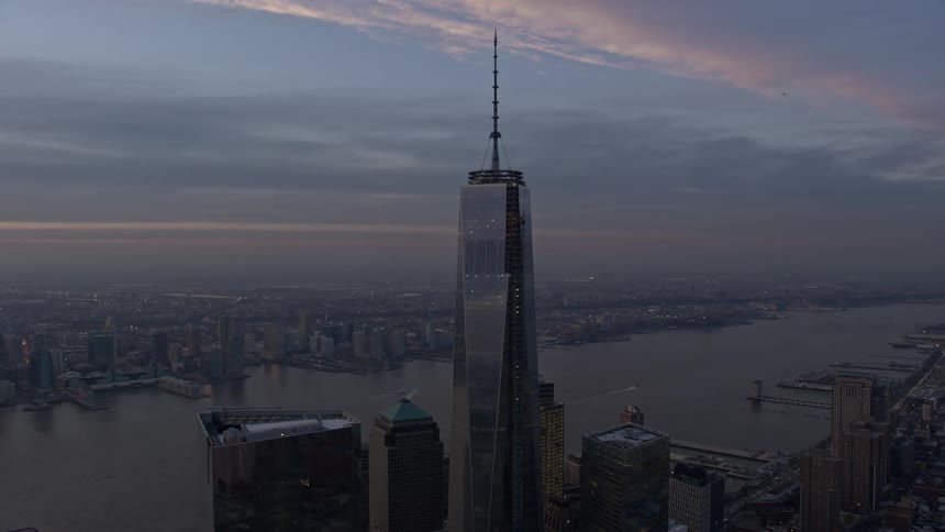 A breathtaking aerial footage capturing the iconic Freedom Tower in downtown Manhattan with the Hudson River in the background during sunset in the winter season