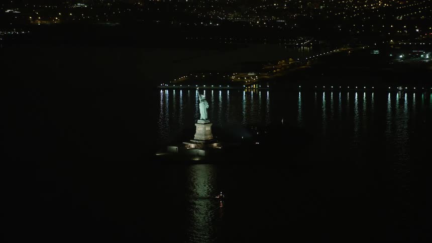 Aerial footage of Statue of Liberty monument and New York City skyline at night during winter